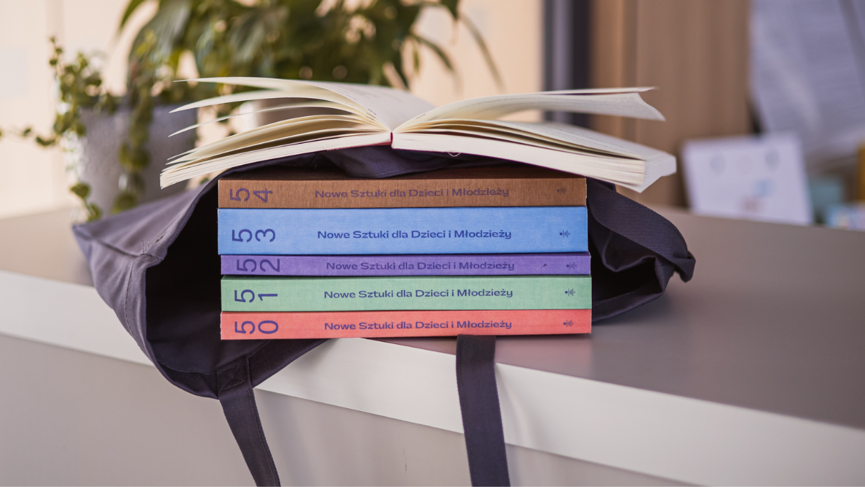 Grzbiety tomów Nowych Sztuk dla Dzieci i Młodzieży włożonych do płóciennej torby.